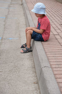 Side view of girl sitting on footpath