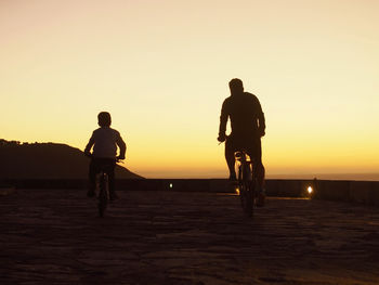 Silhouette man riding bicycle on street against sky during sunset