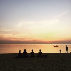 People at beach against sky during sunset