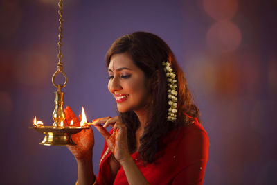 Beautiful indian woman in red sari lighting diya during diwali