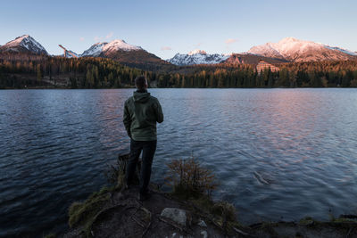 Rear view of man standing on lake against mountain