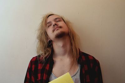 Man with long blond hair against wall