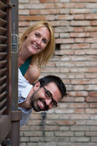 Portrait of smiling young woman standing against brick wall