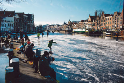 People on frozen river in a city against sky