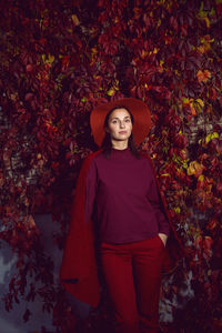 Woman in a red hat and red sweater stands on a background of orange leaves grapes wall autumn