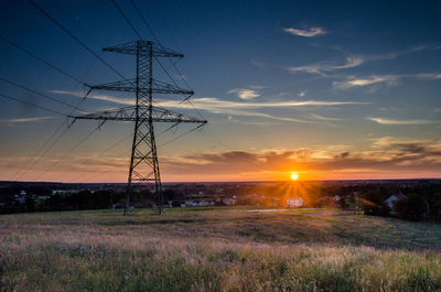 Electricity pylon on field against sky at sunset