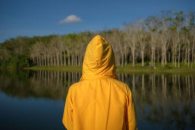 Rear view of woman standing by lake against trees