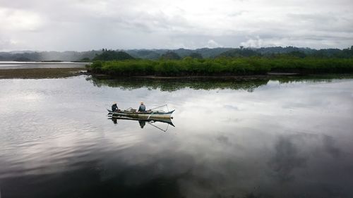 Boat sailing in lake against cloudy sky