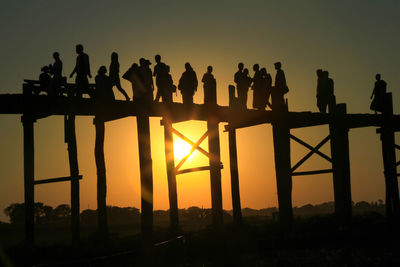 Silhouette people on bridge against sky during sunset