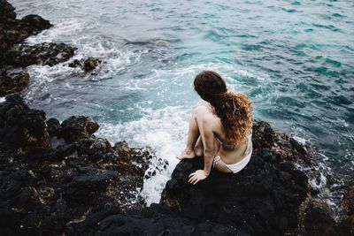 High angle view of woman sitting on rock at sea shore