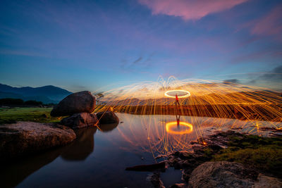 Man standing under wire wool at lakeshore against sky during sunset