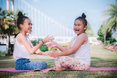 Portrait of sisters playing while sitting on exercise mat against clear sky at park