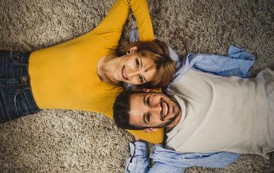High angle portrait of smiling young couple lying on carpet