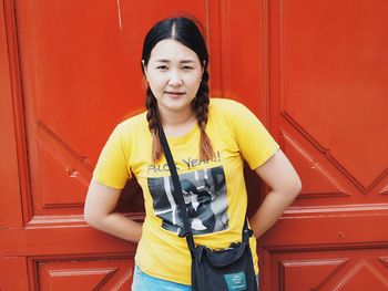 Portrait of smiling young woman standing against yellow door