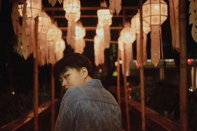 Rear view of man looking at illuminated lamp at night