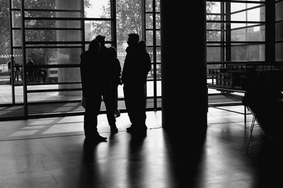 Silhouette people standing by window