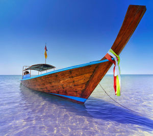 Longtail boat moored in sea against clear blue sky