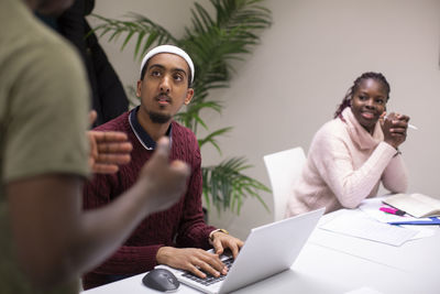 Student with laptop looking at teacher explaining in classroom