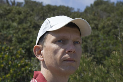 Thoughtful man wearing cap against trees