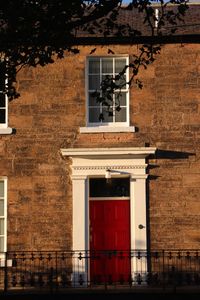 Front elevation of sandstone georgian house with red front door and white sash and case windows 