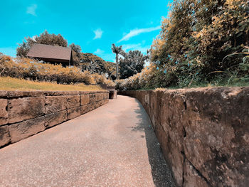 Footpath by wall against blue sky