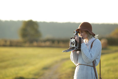 Woman photographing through camera while standing on field