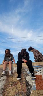 Women sitting on rock against sky