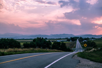 Road by trees against sky during sunset