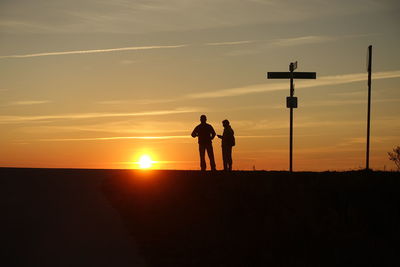 Silhouette people standing on street against sky during sunset