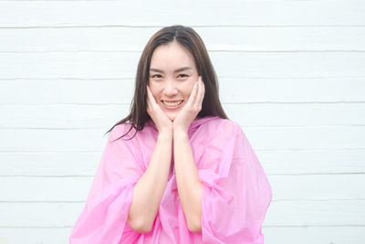 Portrait of smiling young woman wearing raincoat against wall