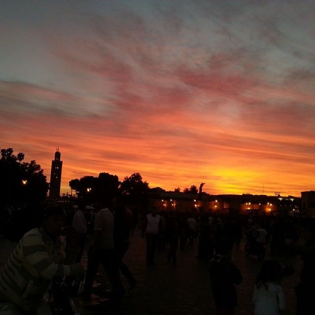 sunset, large group of people, sky, silhouette, orange color, lifestyles, illuminated, cloud - sky, leisure activity, men, person, built structure, dusk, architecture, building exterior, tree, crowd, city, outdoors