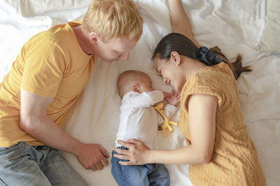 Mother and father playing with toddler on bed at home
