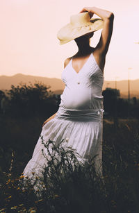 Midsection of woman standing on field against sky during sunset