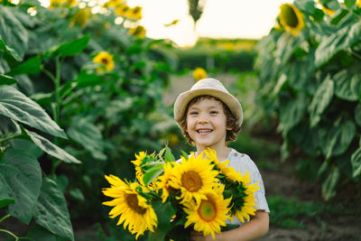 Happy boy walking in field of sunflowers. child playing with big flower and having fun.