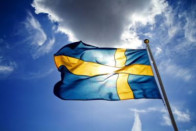 Low angle view of swedish flag waving against blue sky