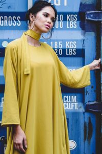 Young woman looking away while standing against yellow wall