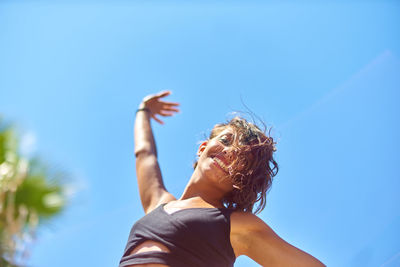 Low angle view of smiling young woman against clear blue sky