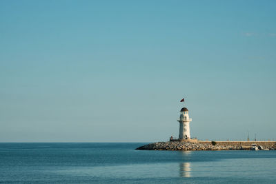 Lighthouse by sea against clear sky