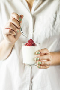 Midsection of woman holding yogurt and raspberries in drinking glass
