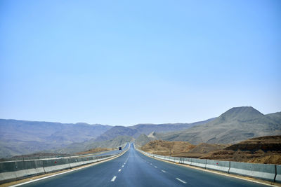 Empty road along landscape against clear blue sky