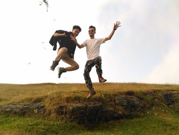 Full length of cheerful friends jumping on field against sky