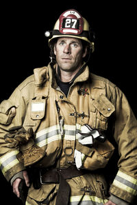 Portrait of firefighter standing against black background