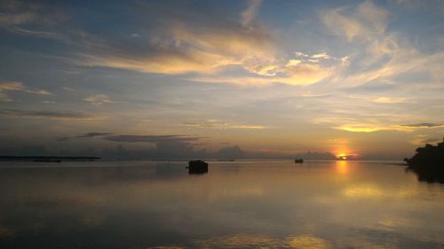 Scenic view of lake against cloudy sky at sunset