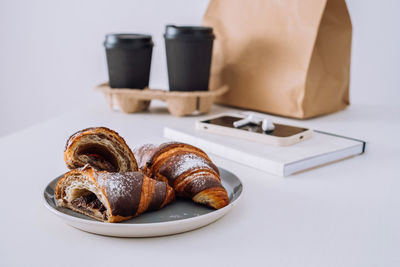 Chocolate croissants with cups of coffee and notepad with smartphone and earphones