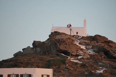 People on rock by building against clear sky