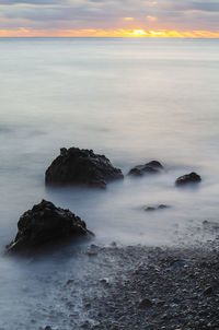 Rock formations in sea at sunset