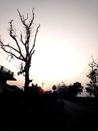 Silhouette bare trees by road against sky during sunset