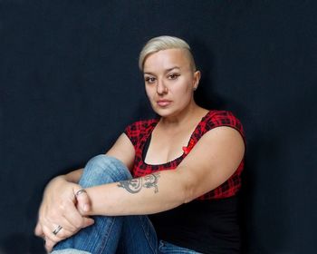 Portrait of confident hipster woman sitting against black background