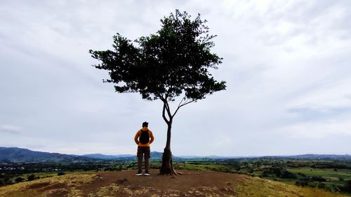 Rear view of man standing by tree against sky