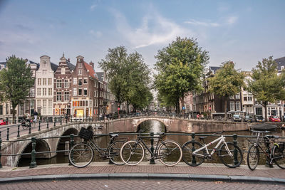 Bicycles on bridge over canal in city against sky